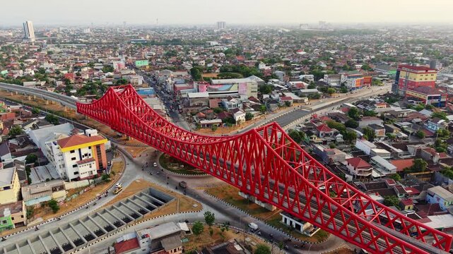 Aerial view of the iconic red Jembatan Kereta Api Joglo railway bridge spanning over the busy urban streets and residential area of Surakarta, Central Java, Indonesia.