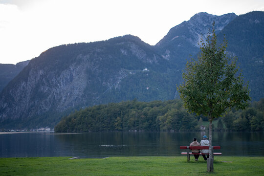 A woman and a man are sitting on a bench on the shore of a mountain lake in Austria.