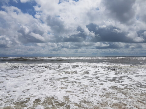 Stormy sea with foamy waves rolling onto the shore under a dramatic sky with heavy white and gray clouds