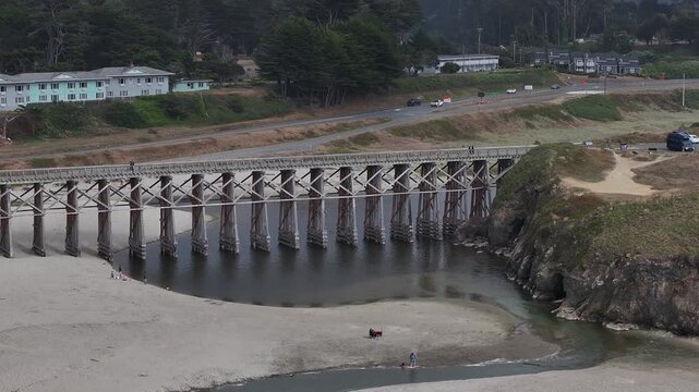 Aerial view of the historic wooden Pudding Creek Trestle spanning the sandy beach and inlet in Fort Bragg, California, United States.