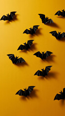 Fototapeta premium Flat lay of black folded paper bats arranged in an expanding arc across a cheerful golden yellow background sharply creased wings casting delicate soft shadows and leaving