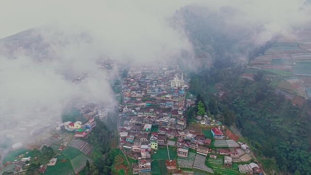 Aerial view of Nepal Van Java village nestled on the slopes of Mount Sumbing, surrounded by terraced vegetable fields and misty clouds in Magelang, Central Java, Indonesia.