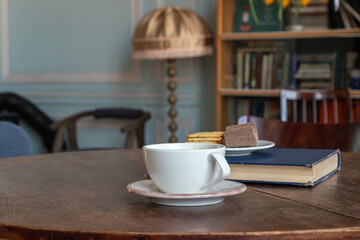 White coffee cup and saucer on wooden table beside a book and cookies. Coffee break and reading moment. Cozy home library interior. Books, leisure and refreshments for a quiet afternoon. © Анастасия Бурлакова