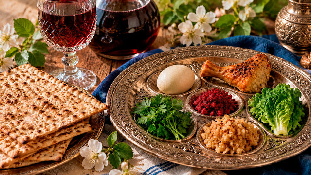 Traditional Jewish Passover Seder plate with symbolic foods. Matzah and red wine on a rustic wooden table with spring flowers. Pesach holiday celebration concept
