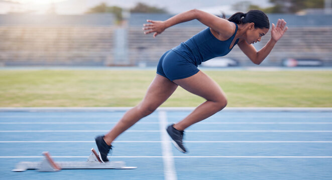 Athletic female runner leaping over a hurdle obstacle during track and field training on sunny stadium track.