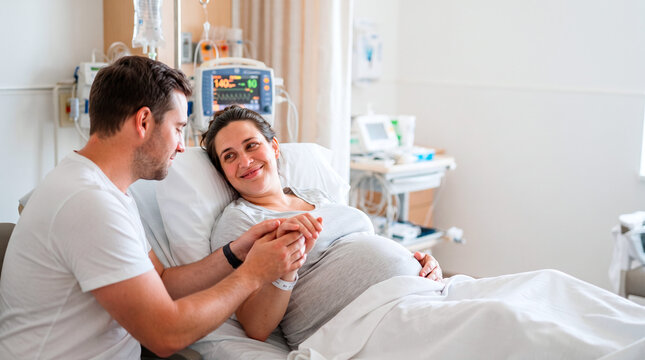 A supportive husband holding his pregnant wife's hand in a modern hospital maternity ward room