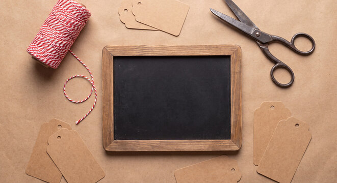 Creative overhead composition of an empty framed chalkboard surrounded by packaging twine craft paper tags and vintage scissors