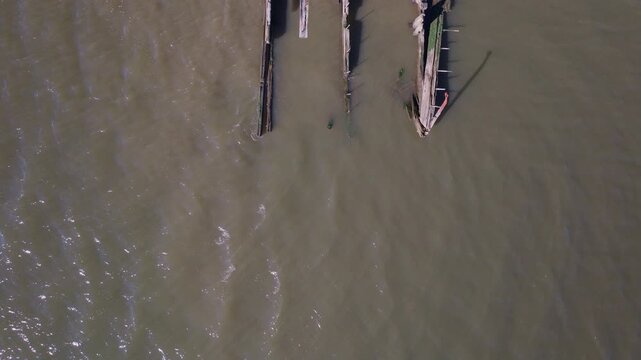 Top down aerial drone view of abandoned wooden pier remains in Arthur Kill near Outerbridge Crossing, Staten Island, New York, showing deteriorating marine structures and tidal water currents