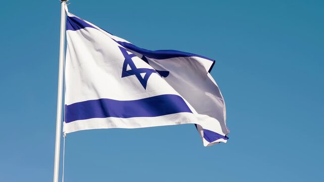 Flag of Israel Waves the Wind. The Big State Flag is illuminated by the sun and flutters epically in the wind against the blue sky