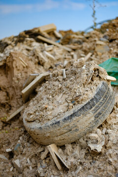 Discarded old car tire half buried in a massive pile of demolition waste and construction rubble polluting the natural environment