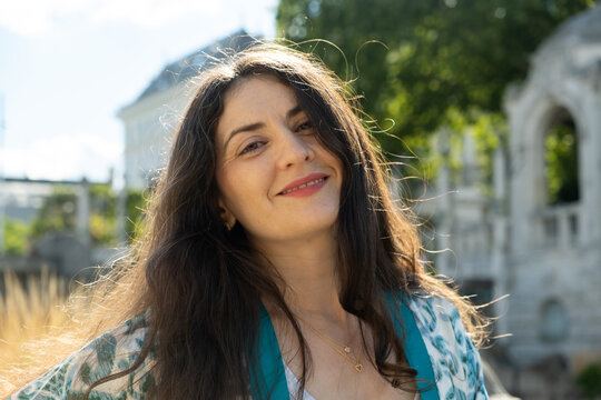 Portrait of attractive 38 year old woman with long hair smiling in city park.
