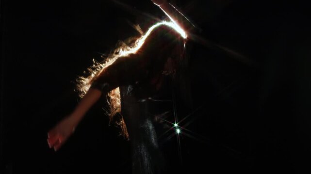 Bright light beam covering the face of a woman in a shiny dress. Anonymous figure, star flare and dark space for themes of energy, insight and change.