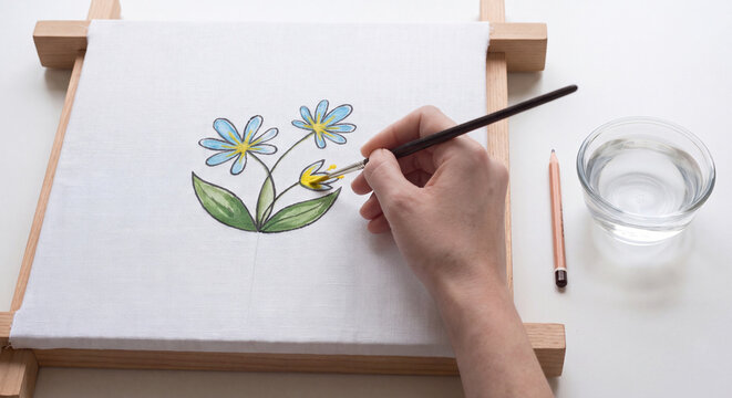 Close up of an illustrator working on floral watercolor artwork by painting botanical stems and leaves with a small precision paint brush