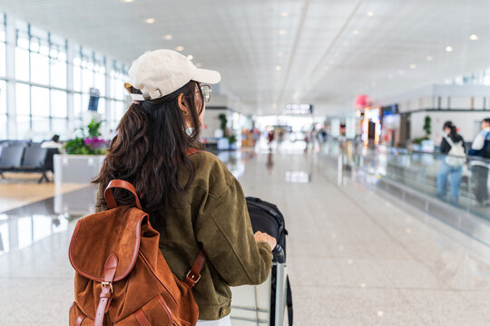 Female tourist passenger pushing a trolley and luggage while looking for her gate at the airport