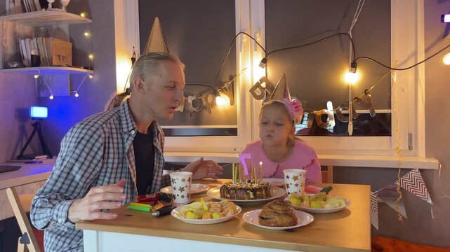 Father and daughter home celebrating birthday together with cake and fairy lights