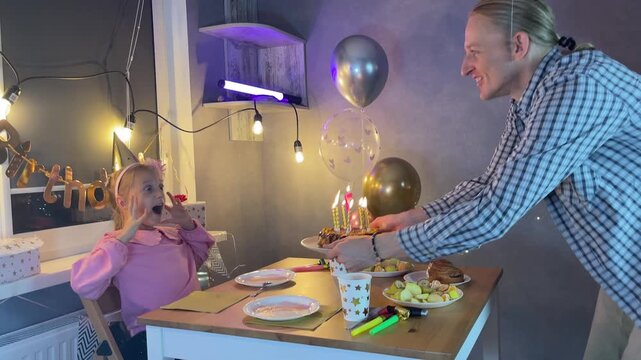Father and daughter home celebrating birthday together with cake and fairy lights