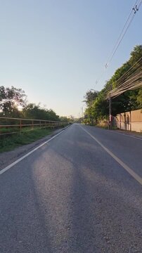 Scenic rural road illuminated by warm golden hour sunlight, with power lines, roadside trees and a bridge creating a peaceful countryside travel scene.