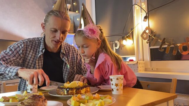 Father and daughter home celebrating birthday together with cake and fairy lights