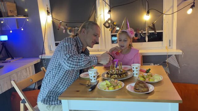 Father and daughter home celebrating birthday together with cake and fairy lights