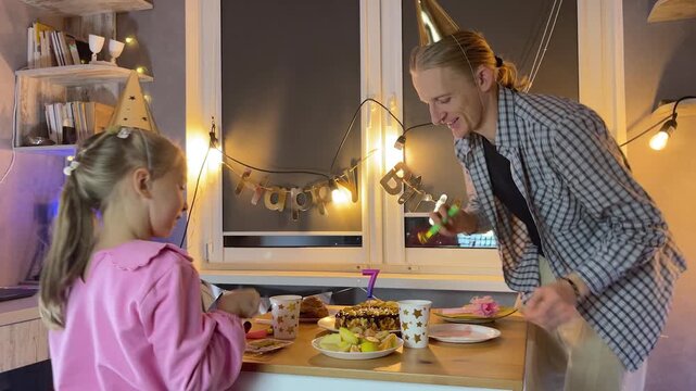 Father and daughter home celebrating birthday together with cake and fairy lights