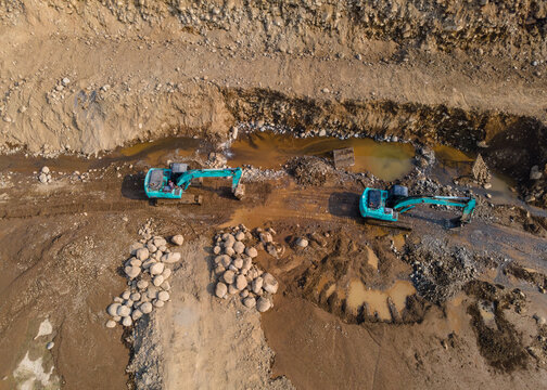 Mining Work of Excavators Operating on Muddy Terrain in a Large-Scale Rock and Sand Quarry in Dawuhan Kulon, Central Java, Indonesia. Heavy Machinery Works Across Wet Ground Viewed from Above.