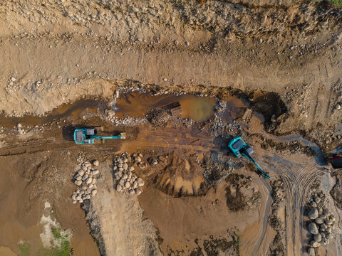 Mining Work of Excavators Operating on Muddy Terrain in a Large-Scale Rock and Sand Quarry in Dawuhan Kulon, Central Java, Indonesia. Heavy Machinery Works Across Wet Ground Viewed from Above.