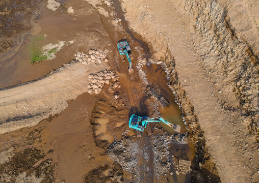 Mining Work of Excavators Operating on Muddy Terrain in a Large-Scale Rock and Sand Quarry in Dawuhan Kulon, Central Java, Indonesia. Heavy Machinery Works Across Wet Ground Viewed from Above.