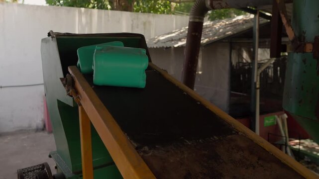 Automatic conveyor belt feeds high-density polyethylene (HDPE) plastic containers into a shredder machine for recycling, part of a sustainable construction materials project.
