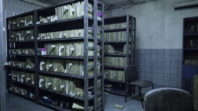 Stark evidence archive with stacked case folders, heavy metal shelving, scattered notes, worn swivel chair, concrete floor stained, harsh overhead lights,