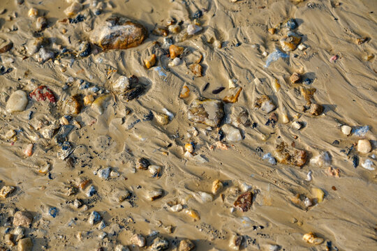 Wet sandy ground texture covered with small pebbles and natural water runoff patterns after heavy rain creating an earthy background