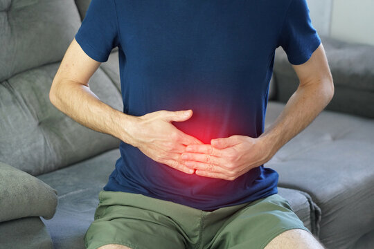 Unrecognizable man massaging bloated belly with flat hands in severe gas pain with red highlight