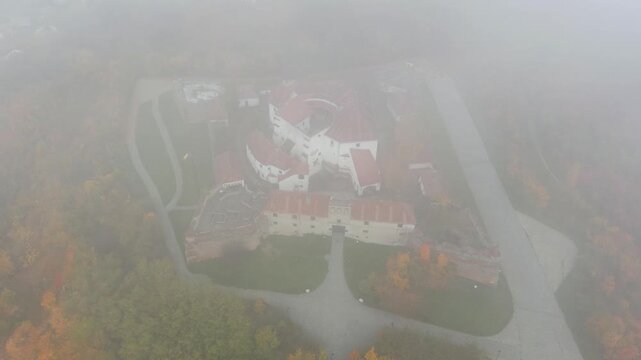 Aerial view of Rasnov Citadel surrounded by autumn trees and fog in Brasov, Brasov, Romania.