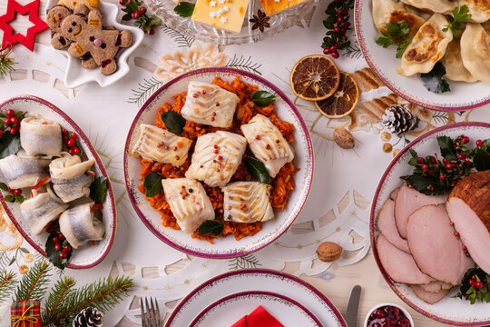Classic Christmas food medley on a decorated table. Fish, dumplings stuffed with cabbage and mushrooms, cheesecake, and ham.