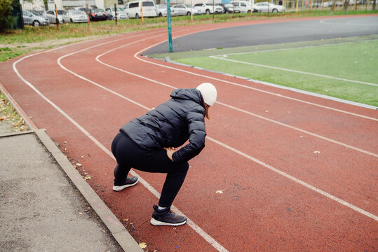Young woman wearing a warm jacket doing stretching exercises on an outdoor running track