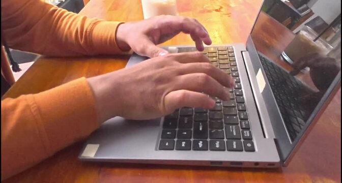 Side view of man hands typing on laptop keyboard at wooden table