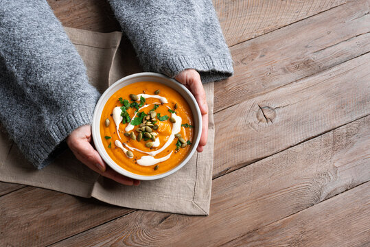 Female hands in knitted sweater holding bowl with pumpkin soup