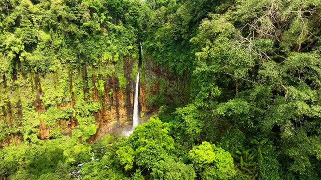 Aerial view of Kapas Biru Waterfall surrounded by lush tropical rainforest in Kecamatan Pronojiwo, Jawa Timur, Indonesia.
