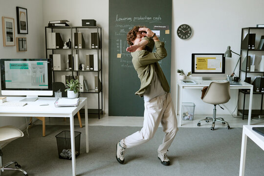 Young adult Caucasian man dancing alone in modern office room, expressing joy and celebration. Ideal for corporate wellness campaigns and workplace culture marketing