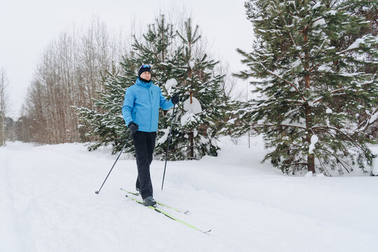 young active skier does skiing in snowy field, sportive caucasian man in blue clothes, ski poles in hands, cloudy winter day, healthy lifestyle