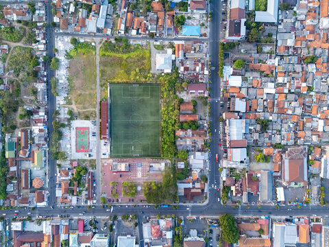 Aerial view of a soccer field surrounded by dense urban housing, rooftops, and streets in Cilacap, Central Java, Indonesia.