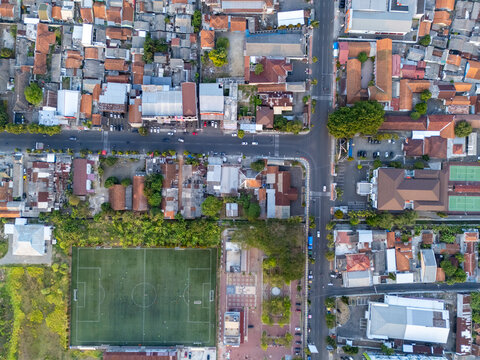 Aerial view of a soccer field situated next to a residential area with dense rooftops and intersecting roads in Cilacap, Central Java, Indonesia.