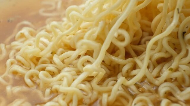 Macro texture of cooked instant ramen noodles floating in broth
