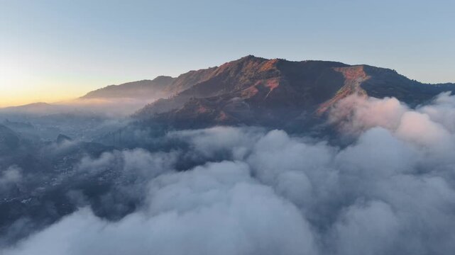 Aerial view of Dieng Plateau mountains rising above a thick sea of clouds at sunrise Indonesia.