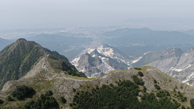 Aerial view of the famous Carrara marble quarries in the Apuan Alps, showing white marble scars on the mountains, rugged terrain, and distant valley views in Carrara, Tuscany, Italy.