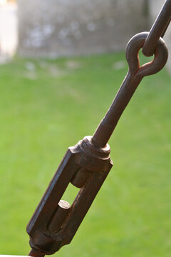 Close-up of a heavy-duty metal turnbuckle and threaded rod on a blurred green background.