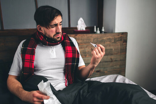 picture from a young man with handkerchief. Sick guy lies in bed and has runny nose. man makes a cure for the common cold. Model male has a high temperature, headache, migraine