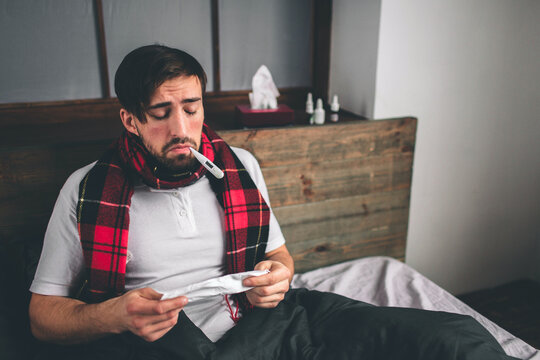 picture from a young man with handkerchief. Sick guy lies in bed and has runny nose. man makes a cure for the common cold. Model male has a high temperature, headache, migraine