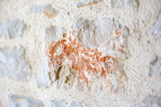 Detailed texture of an aged rustic stone wall with weathered white mortar plaster revealing exposed reddish terracotta brick fragments