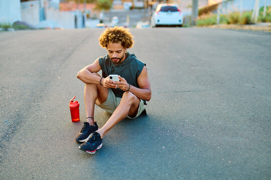 Man checks his phone while exercising outdoors near the beach during sunset, enjoying a moment of relaxation and fitness