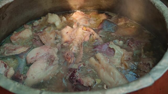 Chef stirring large chunks of meat for plov in a boiling traditional cauldron